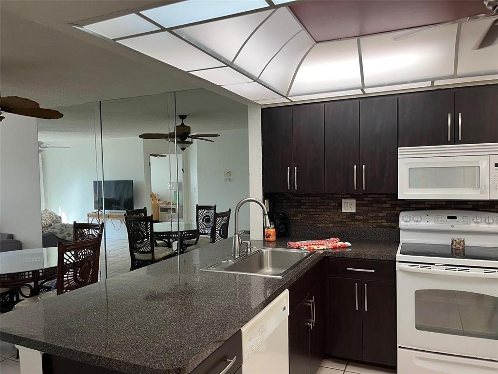 23465 Harbor View Road, Unit 1006 Punta Gorda, FL 33980 - Photo 12 of 41 a kitchen with a stove a sink a kitchen island with chairs and wood cabinets