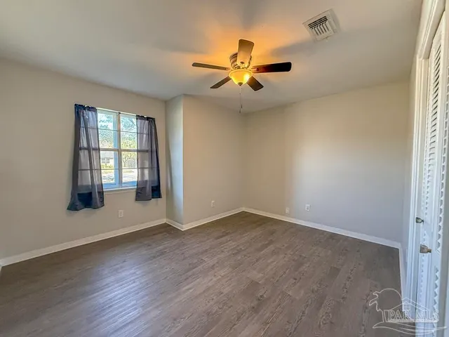 an empty room with wooden floor fan and windows