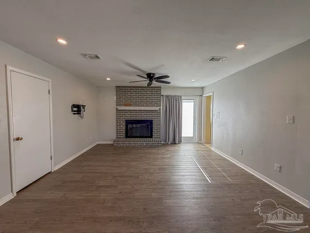 an empty room with wooden floor fireplace and windows