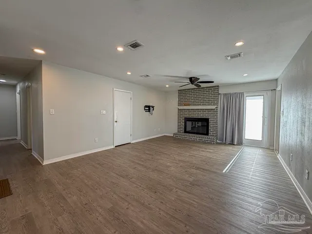 a view of an empty room with wooden floor fireplace and a window