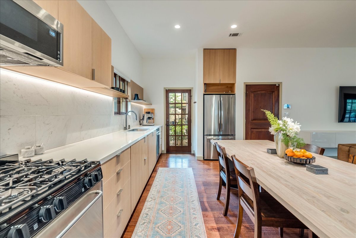 3012 South 4th Street, Unit B Austin, TX 78704 - Photo 9 of 40 Modern kitchen featuring light wood-finish cabinetry, stainless steel appliances, a gas range with an overhead microwave, and integrated under-cabinet lighting