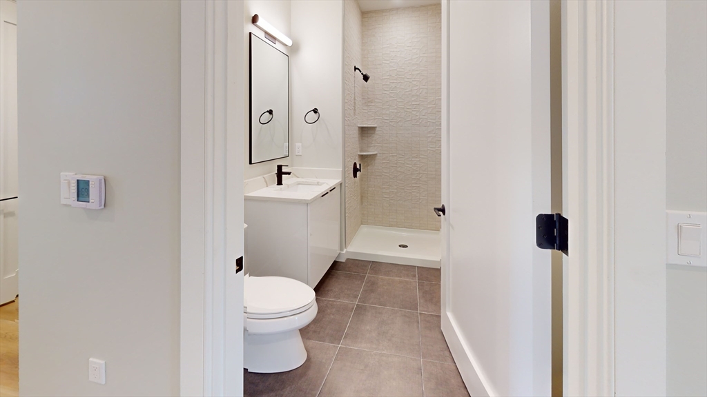 211 Green Street, Unit 509 Boston, MA 02130 - Photo 14 of 20 a bathroom with a granite countertop toilet a sink a mirror and shower