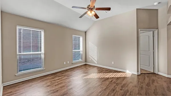 an empty room with wooden floor chandelier fan and windows