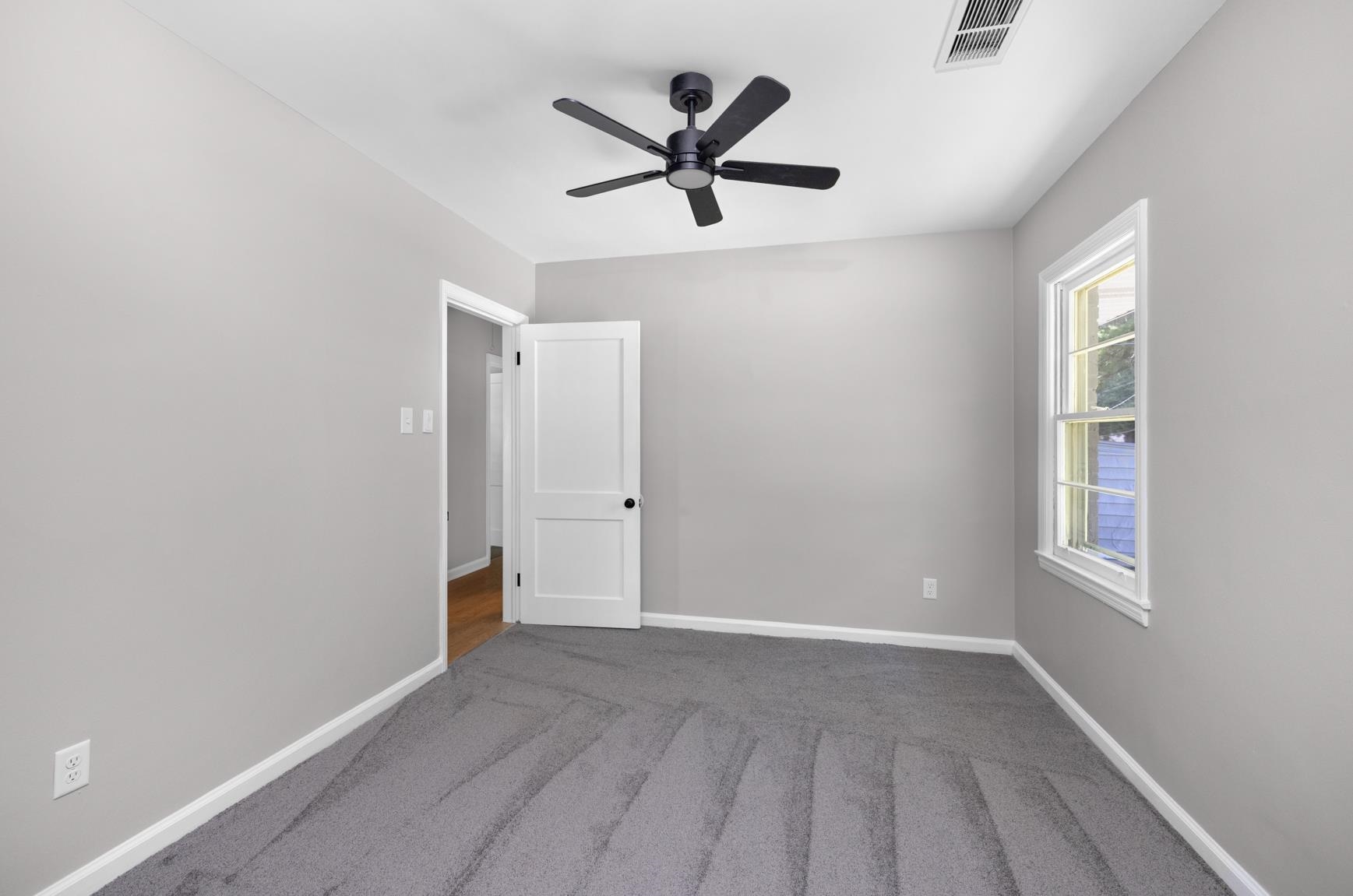 7662 Marvin Road Millington, TN 38053 - Photo 14 of 20 Neutral gray wall finish with a white ceiling, featuring gray carpeting, a multi-pane window with white trim, a white paneled door with black hardware, and a black ceiling fan