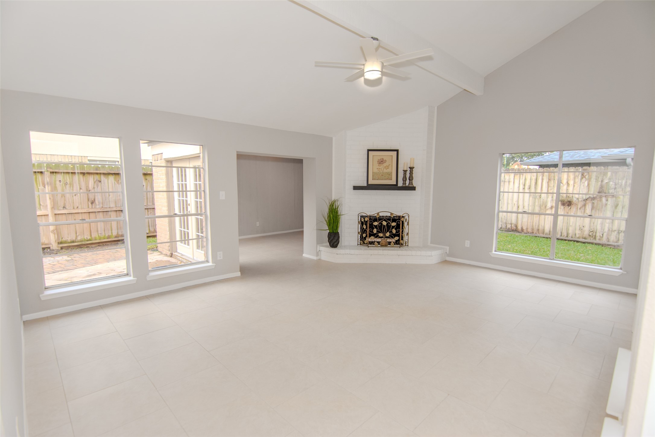 6703 Stonewater Houston, TX 77084 - Photo 11 of 30 Bright and spacious living room with large windows, neutral walls, and a central fireplace. The high ceiling and ceiling fan enhance the airy feel, and there's a view of the fenced backyard.