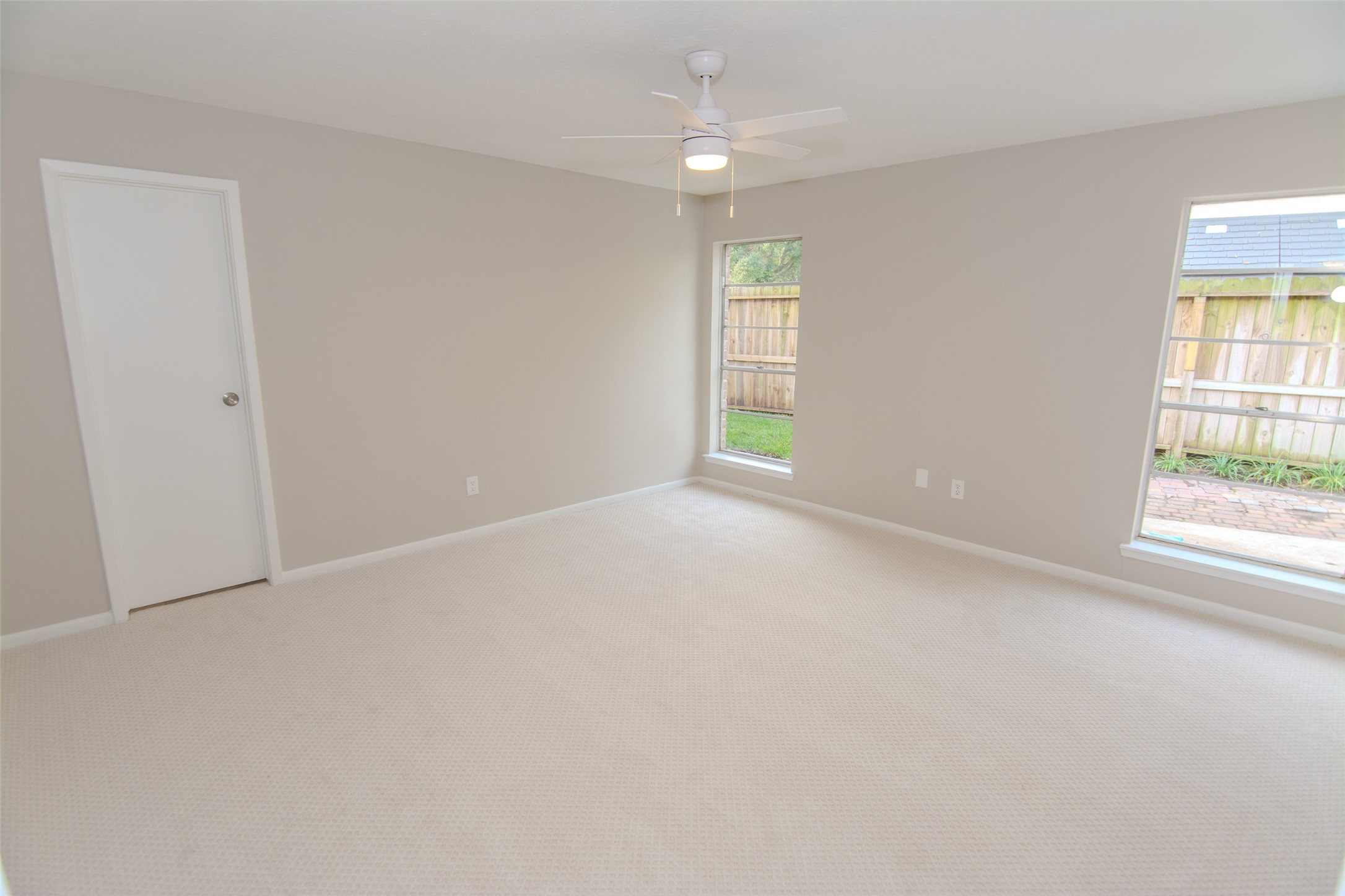 6703 Stonewater Houston, TX 77084 - Photo 16 of 30 Primary bedroom features neutral walls and carpet, a ceiling fan, and two large windows overlooking a fenced backyard.