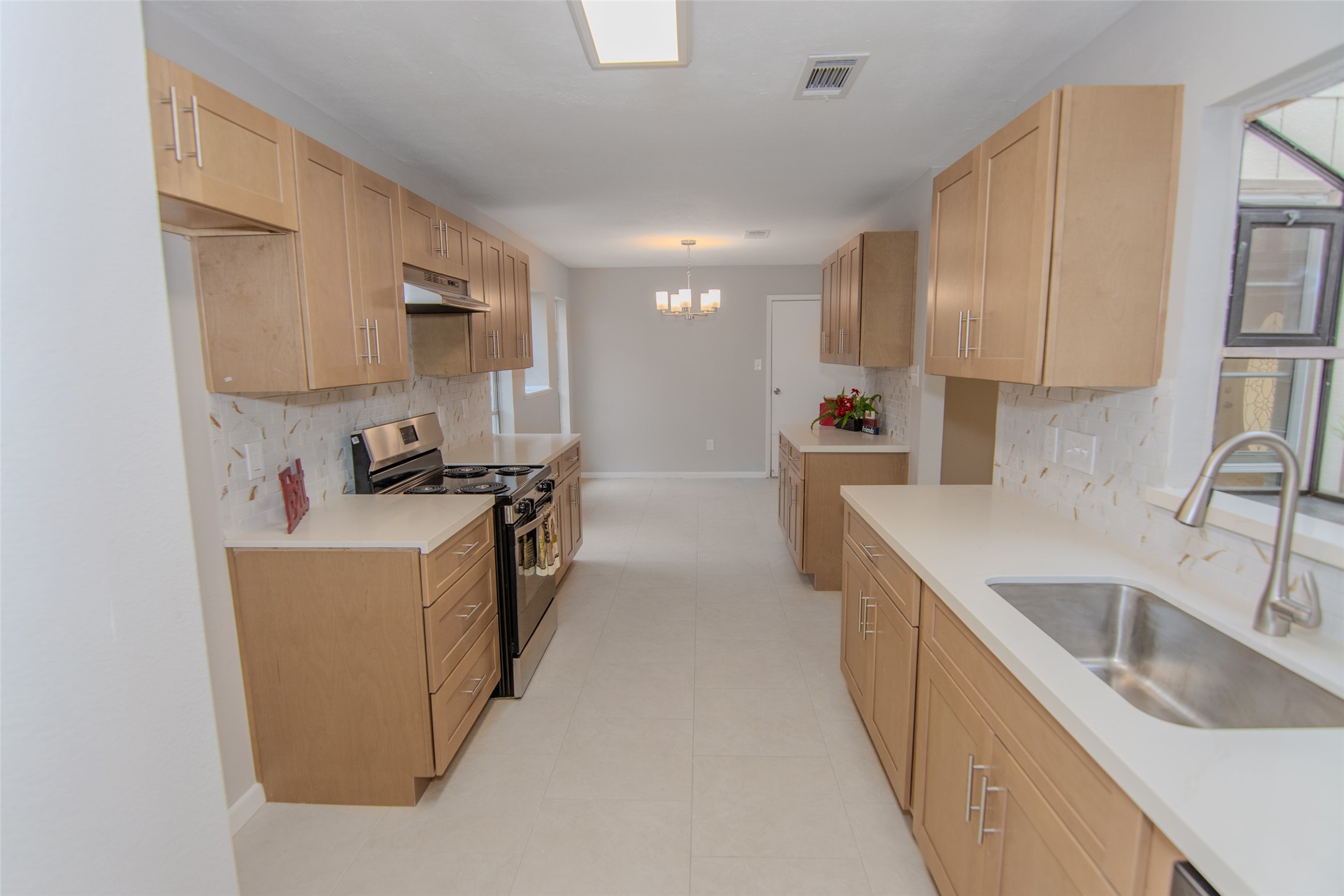 6703 Stonewater Houston, TX 77084 - Photo 2 of 30 Your kitchen features a galley layout with light wood cabinets, a modern stainless-steel stove, and a single basin sink. It has ample counter space, a neutral tile floor, and a contemporary light fixture, creating a bright and functional cooking area.