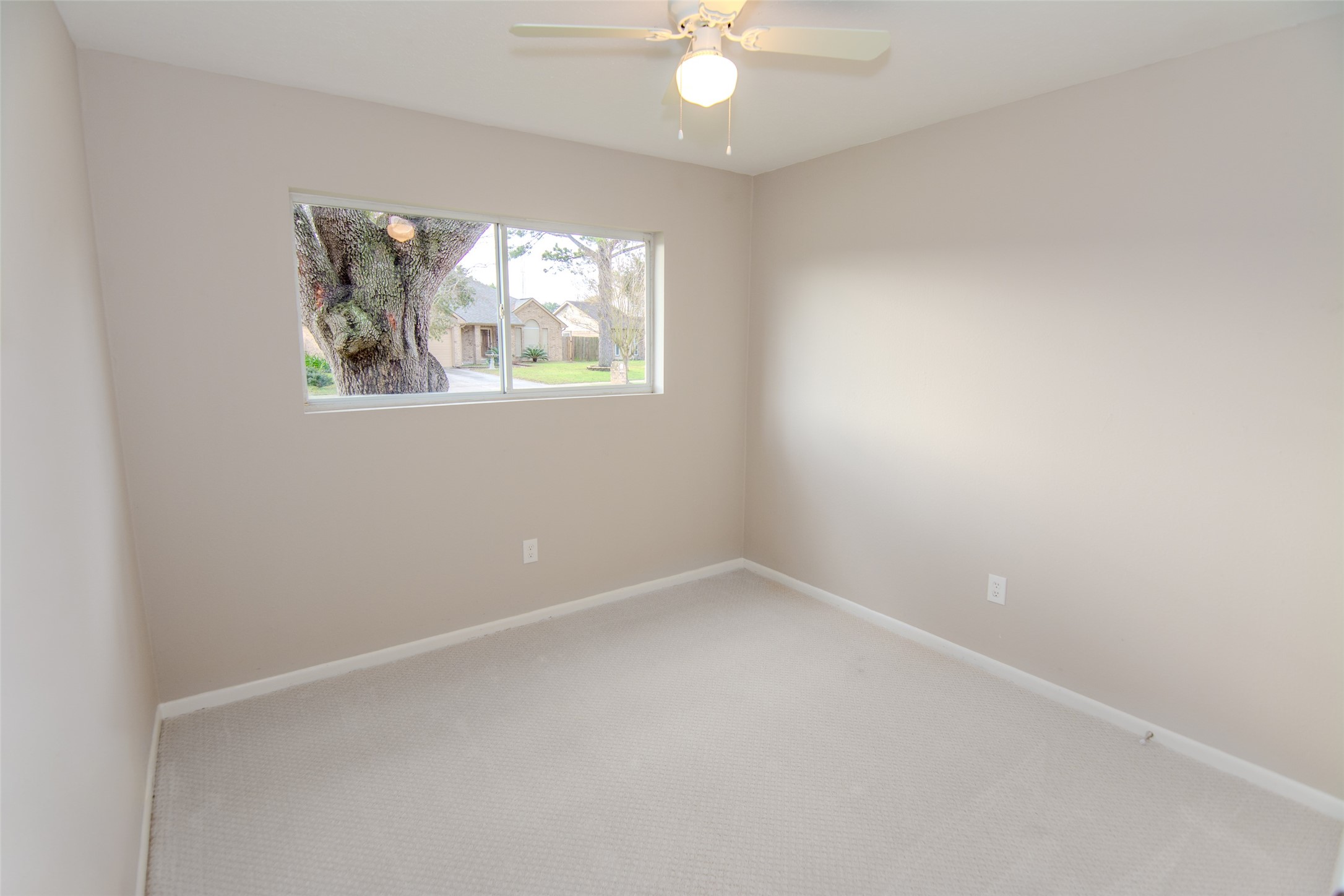 6703 Stonewater Houston, TX 77084 - Photo 22 of 30 Bedroom 4 with neutral walls and designer carpet, featuring a ceiling fan and a window overlooking a tree-lined street.