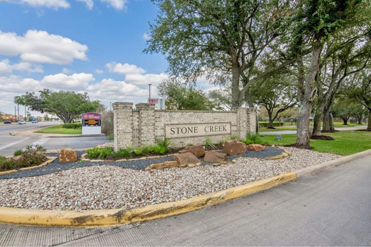 6703 Stonewater Houston, TX 77084 - Photo 26 of 30 Welcome to Stone Creek, a picturesque community entrance featuring a stone sign surrounded by well-maintained landscaping with rocks and greenery. The area is lined with mature trees, creating a serene and inviting atmosphere.