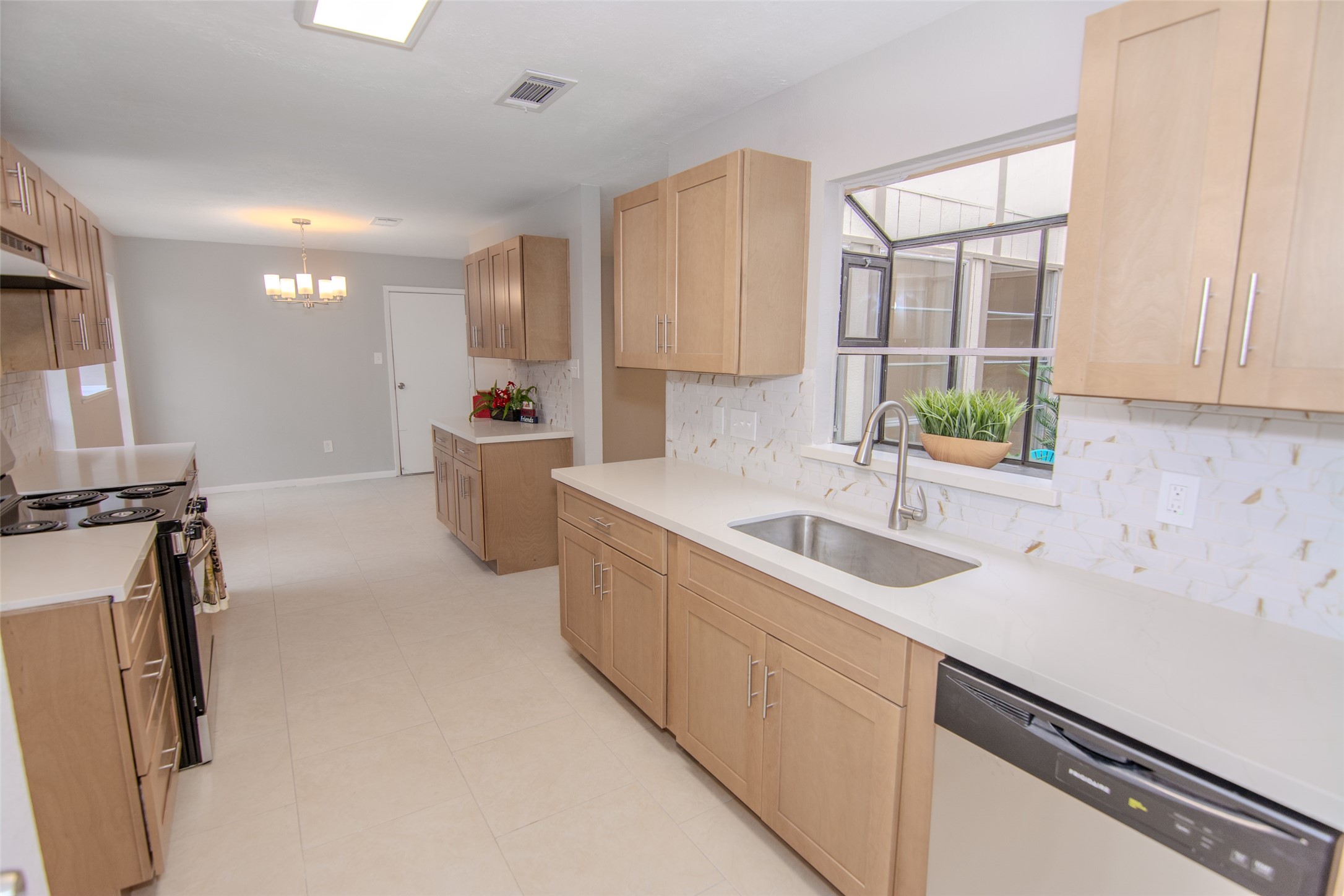 6703 Stonewater Houston, TX 77084 - Photo 3 of 30 Modern galley design with light wood cabinets, sleek countertops, and stainless-steel appliances. A large window offers natural light, and there's a cozy dining area with a contemporary chandelier.