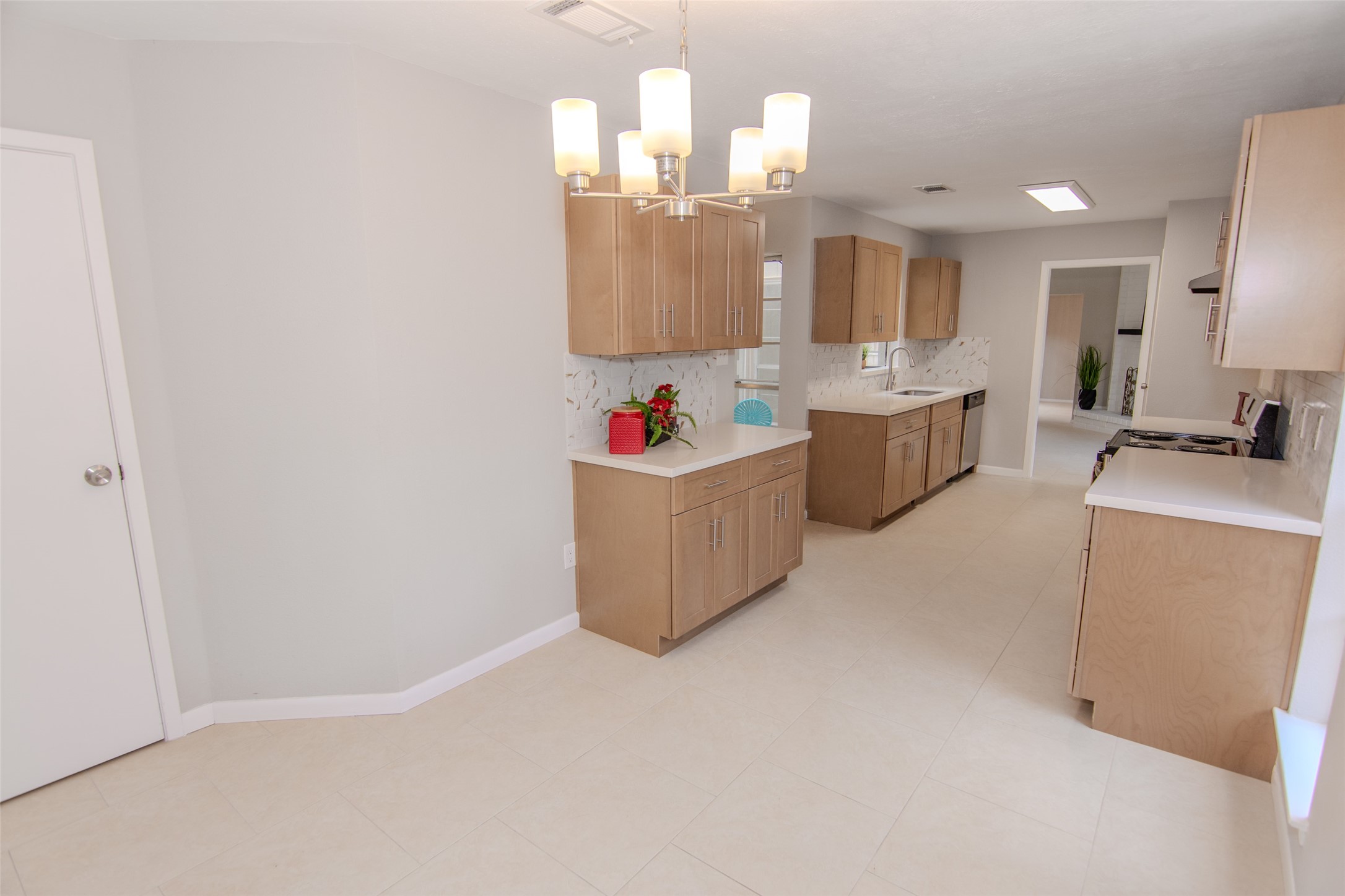 6703 Stonewater Houston, TX 77084 - Photo 6 of 30 This kitchen features a modern design with light wood cabinets, Quartz countertops, and updated appliances. It offers ample space for cooking and dining, complemented by a contemporary light fixture and neutral tile flooring.