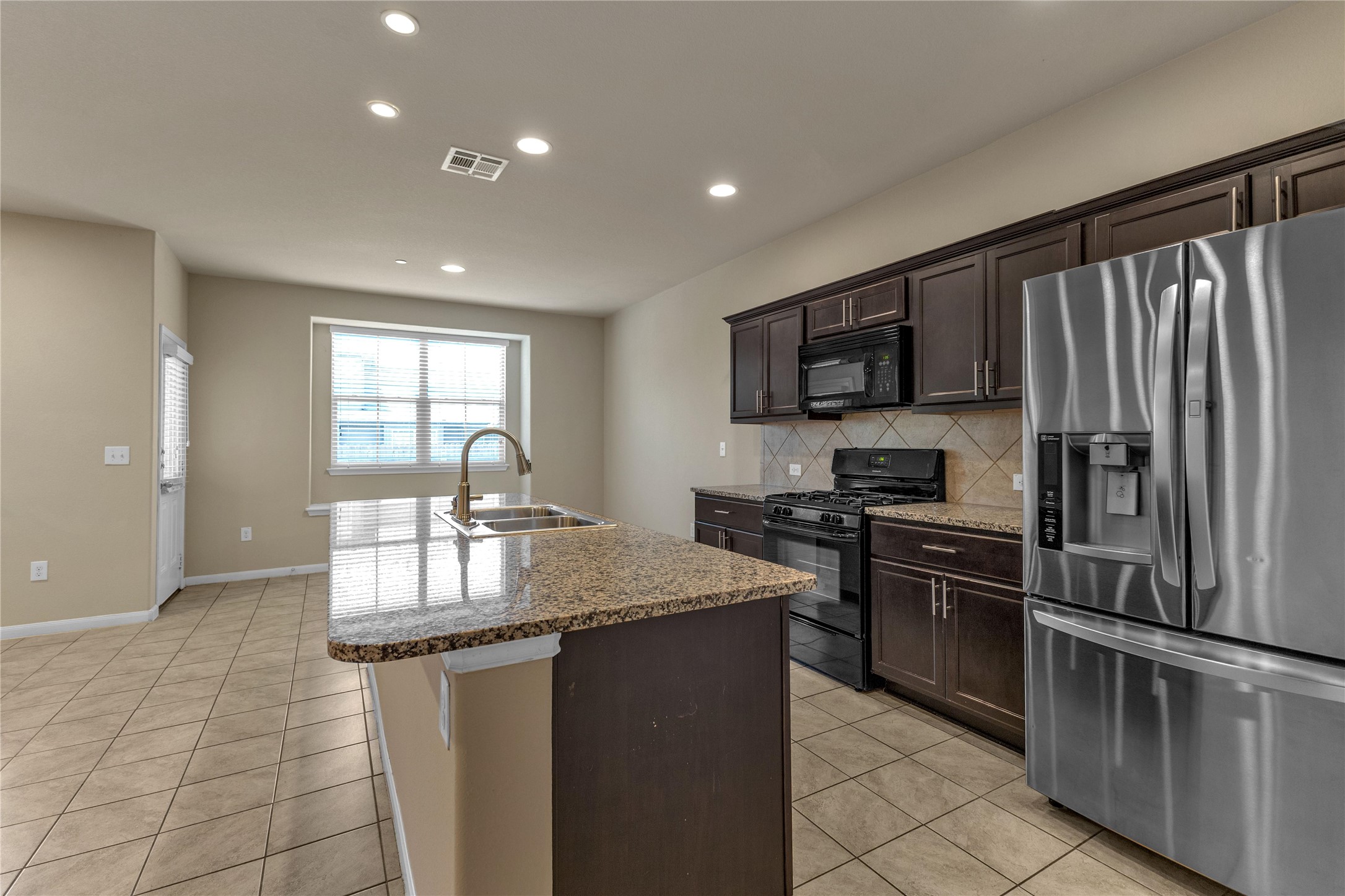 2880 Donnell Drive, Unit 2003 Round Rock, TX 78664 - Photo 10 of 31 Kitchen featuring an island with a double basin sink and granite countertop, dark wood-finish cabinetry, stainless steel refrigerator, and recessed lighting