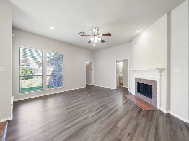 an empty room with wooden floor fireplace cabinet and windows