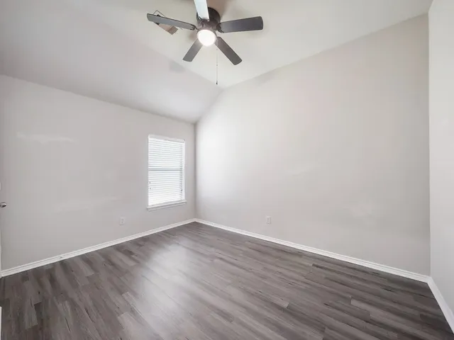 an empty room with wooden floor ceiling fan and windows