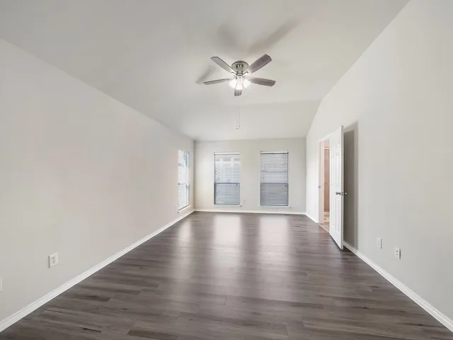 a view of an empty room with wooden floor and a ceiling fan
