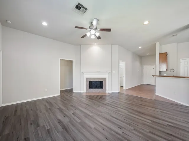 a view of an empty room with wooden floor a fireplace and a window