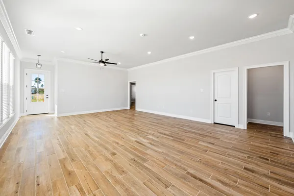 an empty room with wooden floor ceiling fan and windows