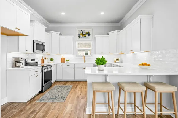 a kitchen with stainless steel appliances granite countertop a stove a sink dishwasher and white cabinets with wooden floor