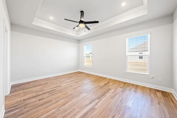an empty room with wooden floor ceiling fan and windows