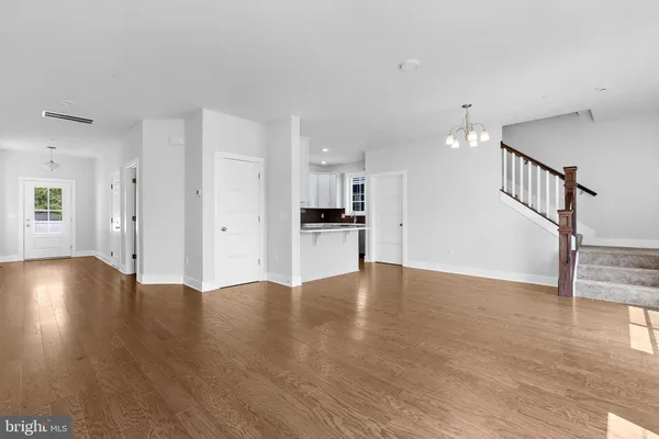 a view of an empty room with wooden floor and a kitchen