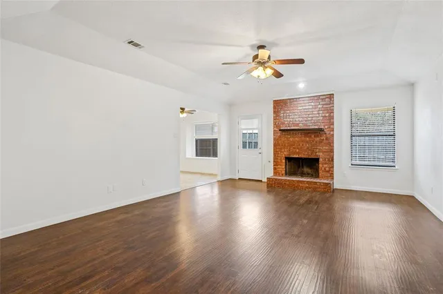 an empty room with wooden floor fireplace and a window