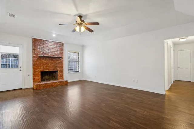 a view of an empty room with wooden floor fireplace and a window