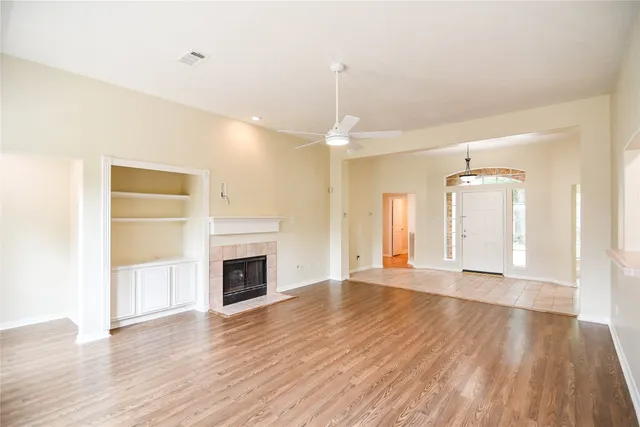 a view of an empty room with wooden floor fireplace and a window