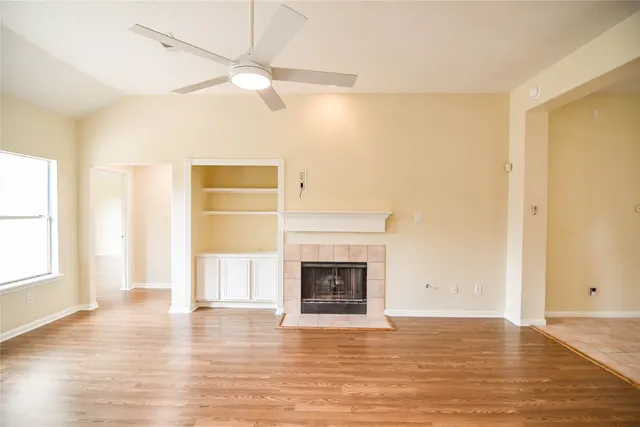 an empty room with wooden floor fireplace and windows