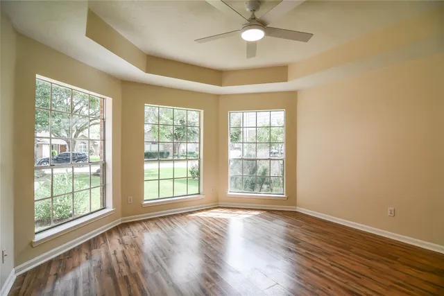 an empty room with wooden floor fan and windows