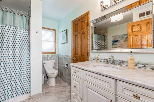 a bathroom with a granite countertop toilet a sink a mirror a window and shower