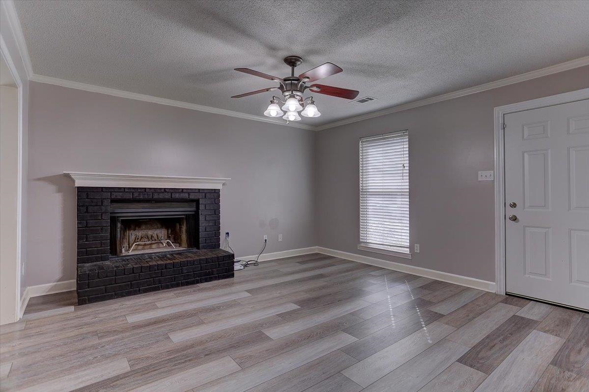 7304 Country Side Road Memphis, TN 38133 - Photo 3 of 18 Unfurnished living room with crown molding, visible vents, a ceiling fan, a fireplace,