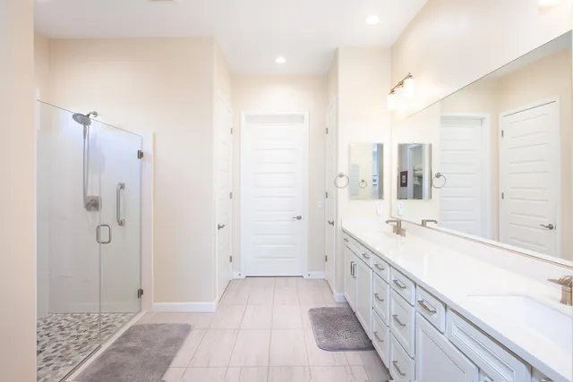 a spacious bathroom with a double vanity sink a large mirror and shower
