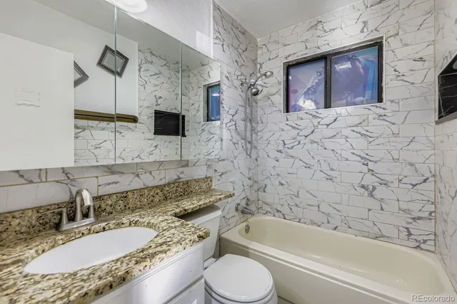 a bathroom with a granite countertop sink toilet mirror and bathtub