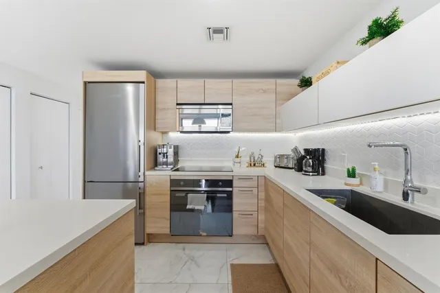 a kitchen with stainless steel appliances a sink a stove a refrigerator and white cabinets