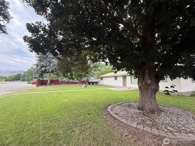 a view of a white house with a big yard plants and large trees
