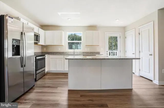 a kitchen with granite countertop a refrigerator a sink dishwasher a stove and white cabinets with wooden floor