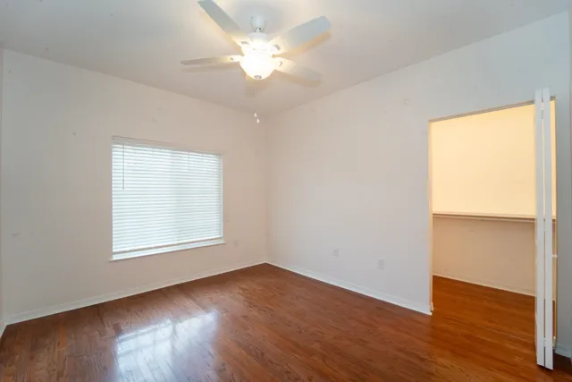 an empty room with wooden floor chandelier fan and windows