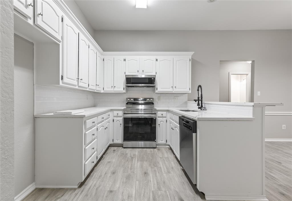304 Moore Creek Road, Unit 300 Hurst, TX 76053 - Photo 4 of 17 Kitchen featuring white cabinetry, light-toned countertops, a white subway tile backsplash, stainless steel appliances, and wood-finish flooring