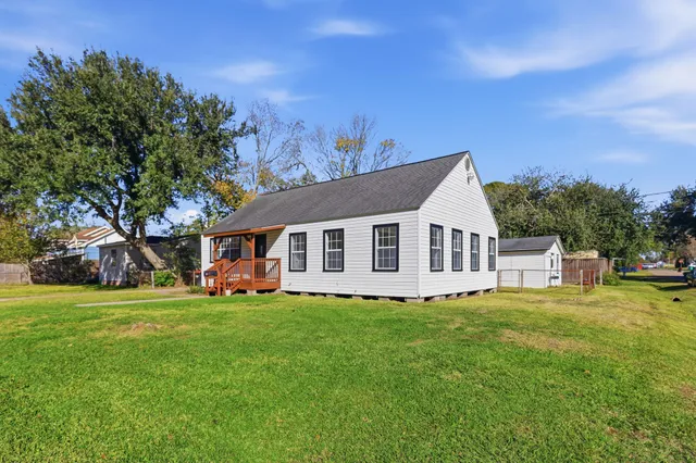 a house that is sitting in the grass with large trees and plants