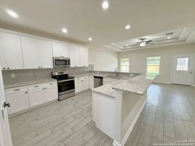 a kitchen with stainless steel appliances granite countertop a stove top oven a sink dishwasher and a refrigerator with wooden floor