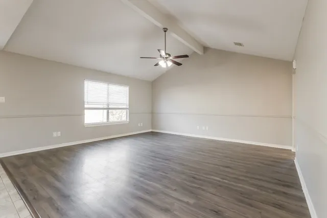 an empty room with wooden floor ceiling fan and windows