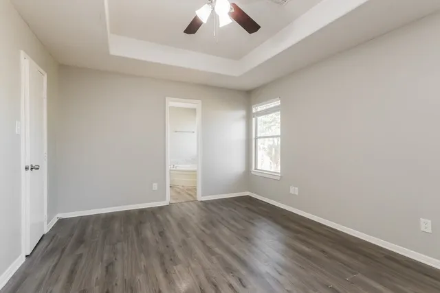an empty room with wooden floor chandelier fan and windows