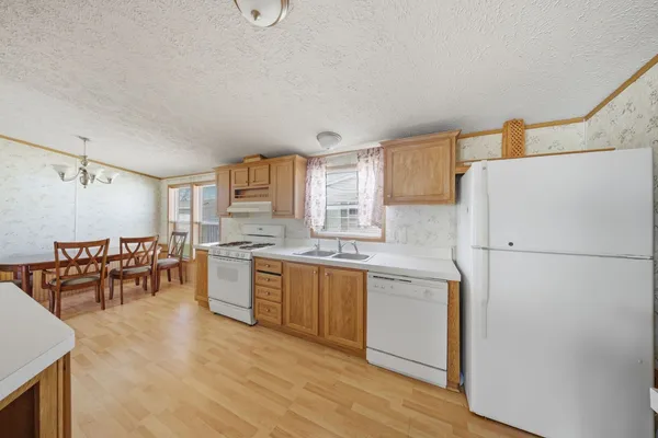 a kitchen with a refrigerator a stove a sink a dining table and chairs with wooden floor