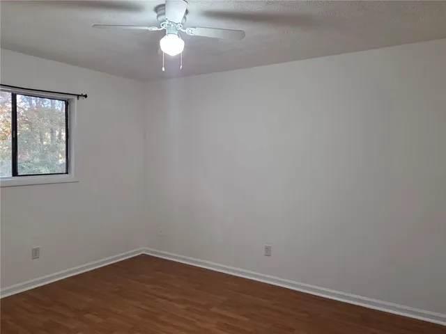 an empty room with wooden floor chandelier fan and windows