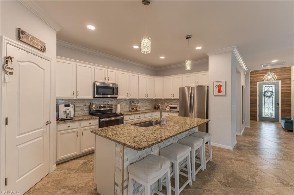 9231 Shadow Oak Lane Naples, FL 34120 - Photo 16 of 46 a kitchen with stainless steel appliances granite countertop a kitchen island a stove a refrigerator a sink a dining table and chairs