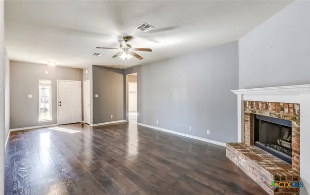 a view of an empty room with wooden floor fireplace and a window