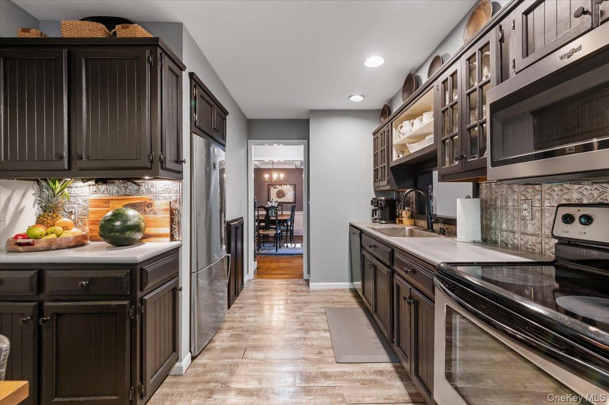 10 Rancher Place Huntington, NY 11743 - Photo 13 of 44 Galley kitchen featuring dark wood cabinetry, stainless steel appliances, light countertops, and wood-finish flooring