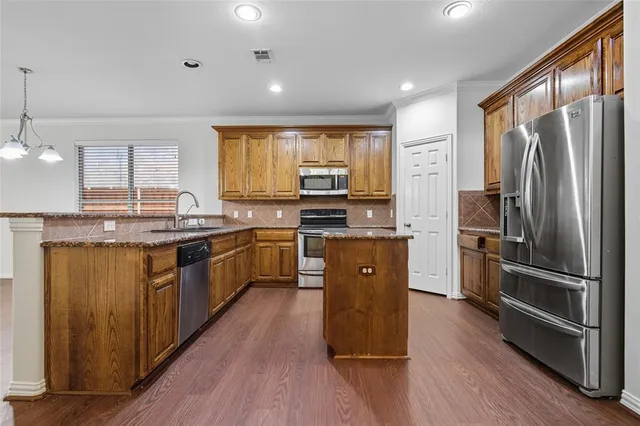 a kitchen with stainless steel appliances granite countertop a refrigerator a stove top oven a sink and dishwasher with wooden floor