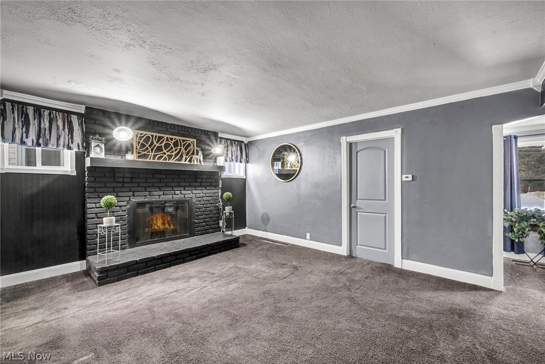 4717 Snow Road Cleveland, OH 44134 - Photo 7 of 30 Unfurnished living room featuring a textured ceiling, carpet floors, a brick fireplace, and ornamental molding