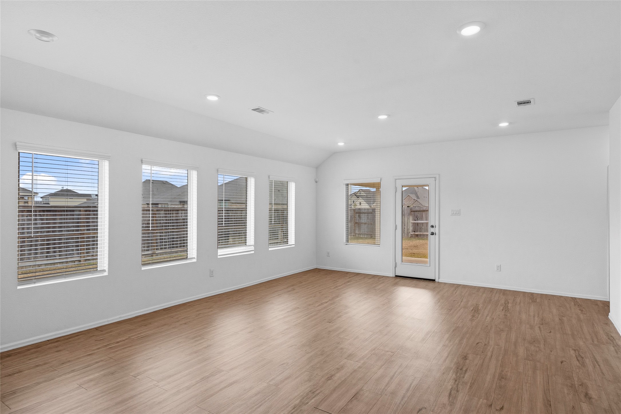 3705 Paloma Fls Lane Rosenberg, TX 77469 - Photo 11 of 27 Spacious living area with wood-look floors, recessed lighting, and a wall of windows for natural light. A glass door and additional windows look out to the backyard.